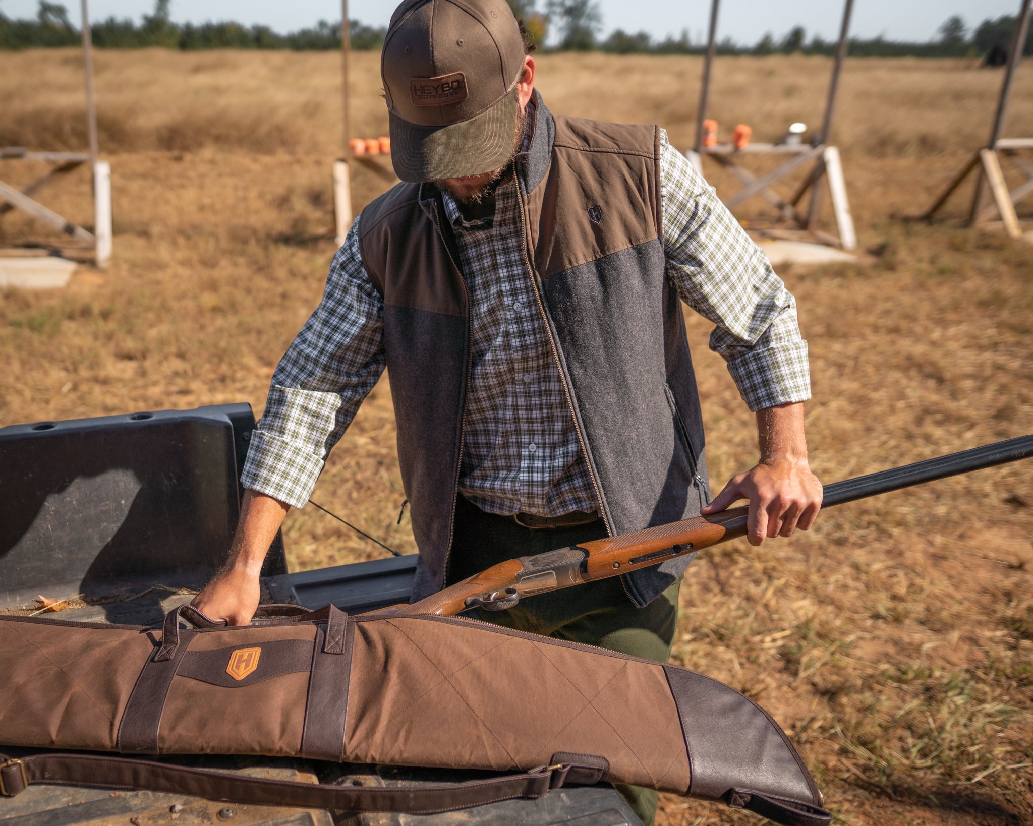man outdoors in flannel and vest placing rifle in a rifle bag